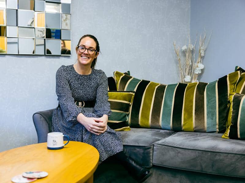 Colleague sat on sofa smiling 