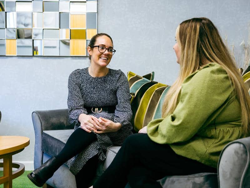 Two colleagues sat on sofa chatting to each other