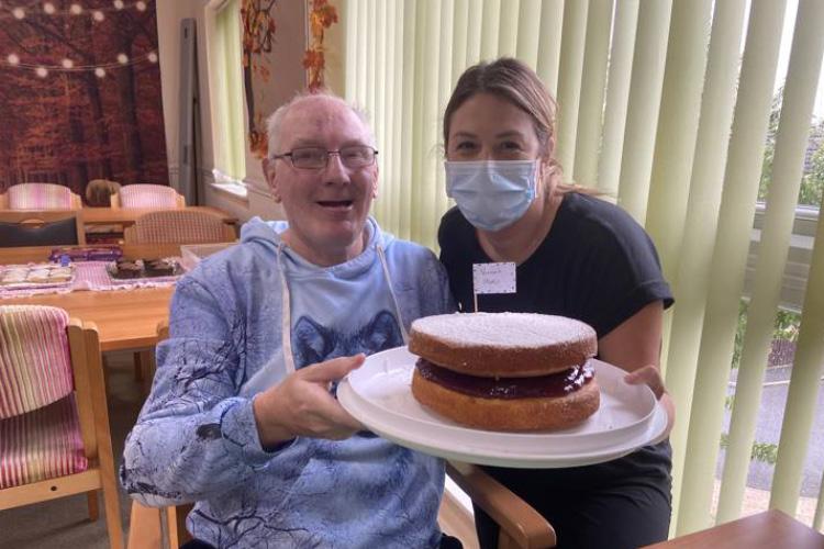 Male service user holding a cake with health care assistant